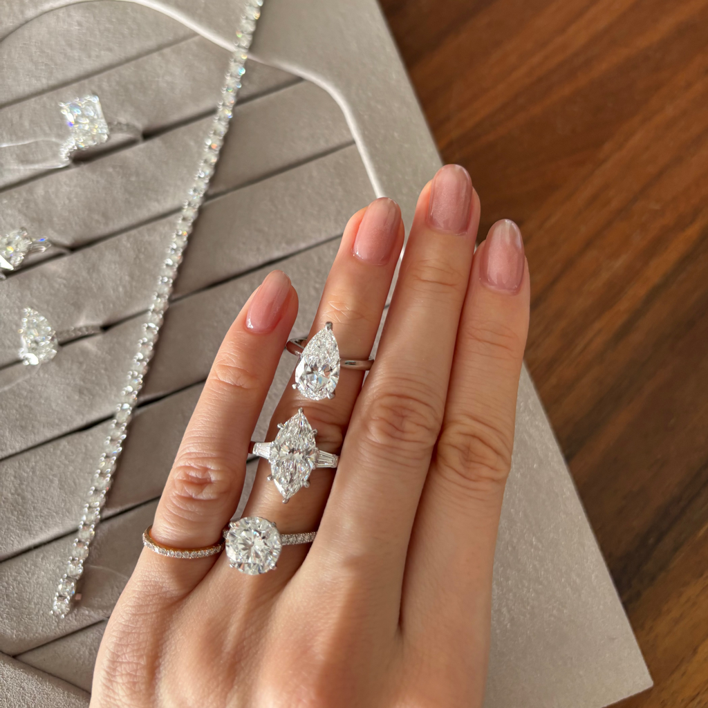 Hand wearing diamond rings with a necklace on a wooden surface